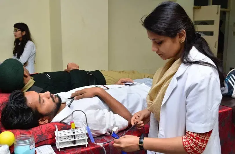 A student in a lab coat attending to a donor at a blood donation camp