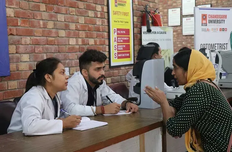 Students in lab coats recording a woman's details at an optometry camp